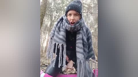 Media: Video of a fair-skinned, bearded man in a gray beanie, gray scarf, and black coat, kneeling in a snowy forest, looking shocked.