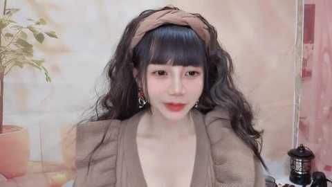 Media: Video of a young Asian woman with long black hair, wearing a beige headband, brown top, and red lipstick, sitting against a floral backdrop.