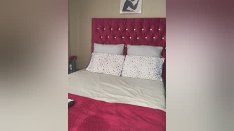 Media: Video of a modern bedroom with a plush, tufted maroon headboard, white pillows, and a beige bedspread. The background wall features a minimalist black and white abstract painting.