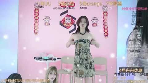 Media: Video of a Chinese woman in a patterned dress, posing in a pink-themed promotional setting with posters and text, featuring a large bottle of hair product.