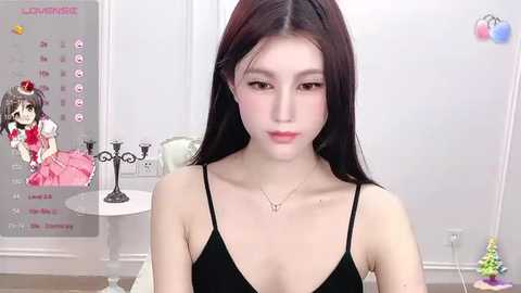 Media: Video of a young Asian woman with long black hair, fair skin, and slender physique, wearing a black spaghetti-strap dress, in a minimalist, white-walled room with a calendar and small decorative items.