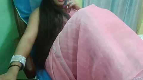 Media: A video shows a pregnant woman with long dark hair, wearing a blue sleeveless top and a pink sari, resting in a chair with a blue cushion, partially covered by a white blanket.