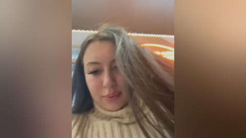 Media: A blurry video of a young woman with light brown hair and a tan sweater, being combed by a hand in a dimly lit room.