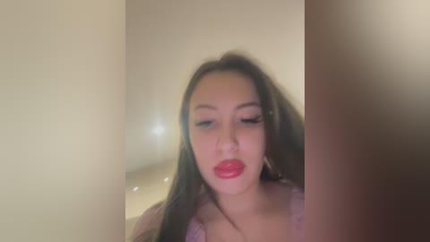 Media: A video of a young Asian woman with long brown hair, wearing red lipstick, and a pink top, blurred and out of focus, possibly taken in a bathroom.