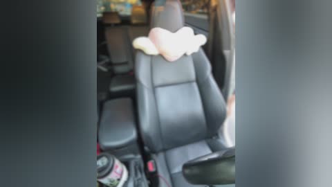 Media: A video shows a black leather car seat with a white fluffy pillow, a pink and white helmet on the floor, and blurred background.