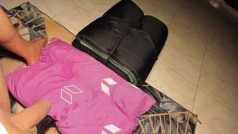 Media: Video of a person folding a bright pink t-shirt and placing it inside a black and green sleeping bag.