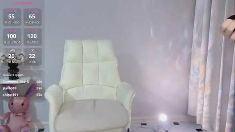 Media: A video depicts a modern, white leather recliner chair with a sleek, minimalist design. The background features a light gray wall and a partially visible, patterned curtain. A digital overlay shows health and fitness metrics on the left side.