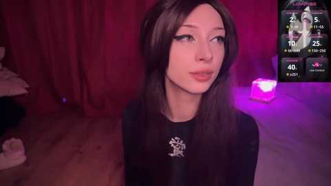 Media: Video of a young woman with long, straight black hair, fair skin, and a slender physique, wearing a black top with a white emblem, in a dimly lit room with red curtains, a glowing pink light, and a digital game interface in the background.