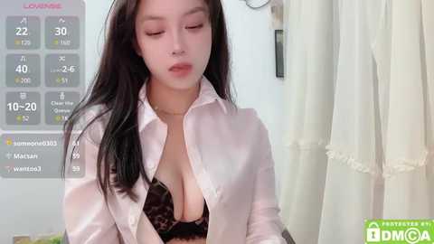 Media: Video of an Asian woman with long black hair, wearing a white button-down shirt, exposing a leopard-print bra, in a dimly lit room with a calendar and curtains in the background.