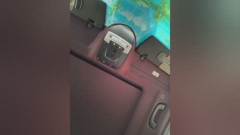 Media: A video of a car interior showing a black navigation screen mounted on a dark maroon dashboard. The background features a blue sky with clouds and green trees, indicating a digital screen displaying a scenic view.