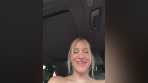 Media: A video of a smiling, topless blonde woman with shoulder-length hair, sitting in a car with dark upholstery and a visible roof handle.