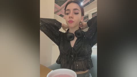 Media: Video of a young woman with medium skin tone, short brown hair, wearing black sequin top, black headphones, and making a pouty face.