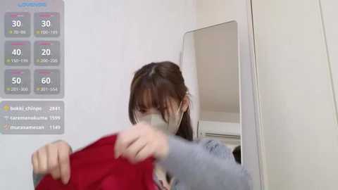 Media: A video of a young woman with long brown hair, wearing a face mask and a red shirt, taking a selfie in front of a mirror, displaying a weather app on the left.