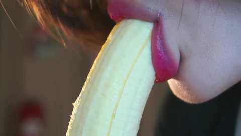 Media: A close-up video of a woman's face, partially visible, with a banana slice in her mouth, highlighting the glossy texture of the banana and her bright red lipstick.