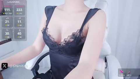 Media: Video of a light-skinned woman in a black lace lingerie bodysuit, seated on a white gaming chair, with a digital interface displaying game stats in the background.