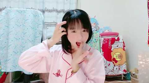 Media: Video of a young Asian woman with short black hair, wearing a pink pajama set, eating a strawberry, surrounded by decorative pillows and a wicker basket in a cozy bedroom.