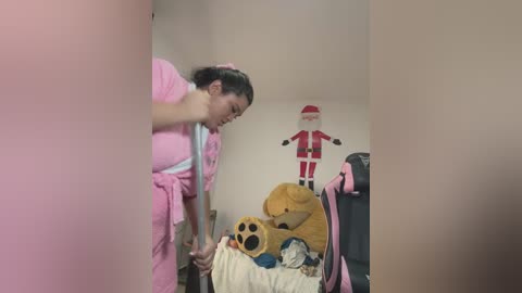 Media: A video shows a young woman in a pink uniform bending over a bed covered with stuffed toys, including a teddy bear and a Santa Claus figure, in a room decorated with holiday-themed decorations.