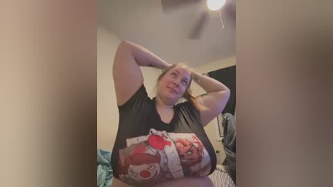 Media: Video of a plus-sized woman with light skin and blonde hair, wearing a black \"The Simpsons\" T-shirt, stretching her arms above her head in a bedroom with a ceiling fan.