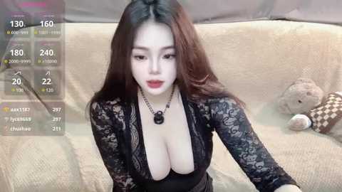 Media: Video of an East Asian woman with long dark hair, wearing a black lace top with a deep neckline, revealing ample cleavage, sitting on a beige couch, surrounded by plush toys.