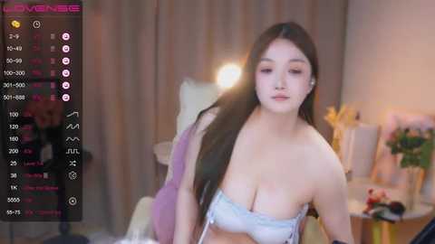 Media: A video of a young Asian woman with long black hair, wearing a light blue bra, taken in a dimly-lit bedroom with soft lighting.