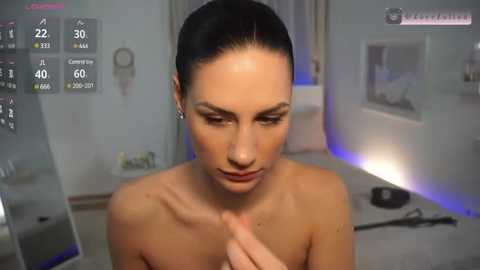 Media: Video of a nude woman with dark hair, fair skin, and slender physique, gazing thoughtfully, with a modern, minimalist room in the background.