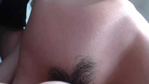 Media: A close-up video of a person's bare back, showcasing light skin and a small patch of dark pubic hair. The background is blurred, with a hint of a black garment.