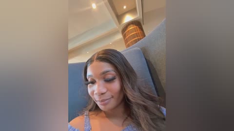 Media: A video of a smiling, light-skinned Black woman with long, wavy hair in a blue top, seated in a modern airplane cabin with beige walls and recessed lighting.