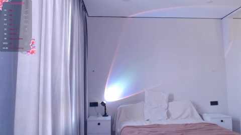 Media: A video of a minimalist, modern bedroom with white walls, a bed with white linens, and a large window casting a rainbow prism effect on the wall.