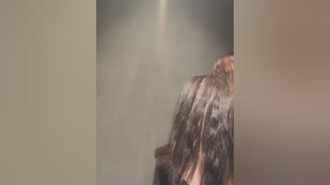 Media: A blurred video of a person's head with dark hair, captured from the side, showing a light-colored wall and ceiling background. The image is soft and out of focus.