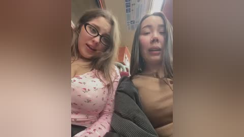 Media: Video of two Caucasian women with light skin, one in glasses, floral top, the other in a beige sweater, sitting close together in a public space.