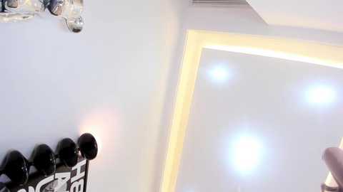 Media: Video of a modern room with white walls, a recessed ceiling light, and a shelf displaying black and white framed artwork. The image is bright, clean, and minimalistic.