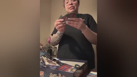 Media: A video of a woman with short dark hair and a black t-shirt, examining a playing card. She's in a well-lit room with a table holding a game box and cards.