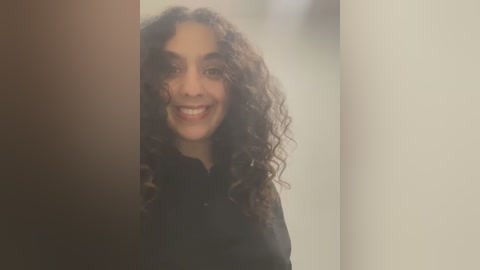 Media: A video of a young woman with curly dark hair, smiling broadly, wearing a black shirt, partially obscured by a dark curtain.