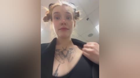 Media: A video of a fair-skinned woman with blonde hair in two buns, wearing a black top, revealing a detailed deer tattoo on her chest.