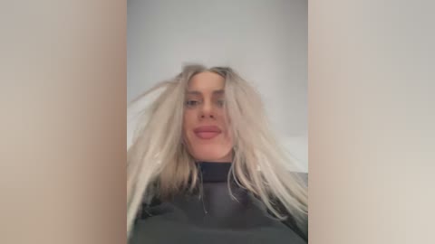 Media: Video of a woman with long, messy platinum blonde hair, wearing a black turtleneck, taken from a low angle, creating a sense of intimacy.