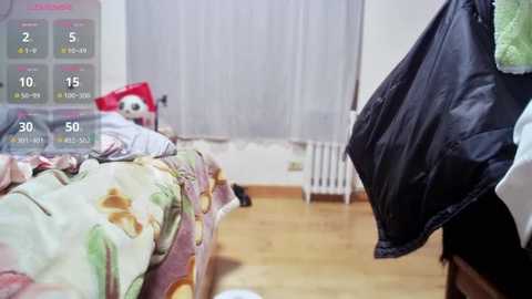 Media: Video of a messy bedroom with a digital time display showing 2:05 AM. A bed with floral sheets, a red pillow, and a black jacket hanging nearby. White curtains and wooden floor.