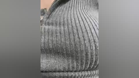 Media: Video of a close-up of a gray ribbed knit sweater, showing textured fabric and a zipper, with blurred background.