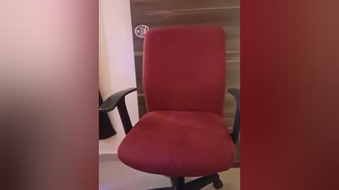 Media: Video of a red office chair with black armrests in a minimalist room with beige walls, featuring a circular white clock on the wall.