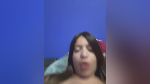 Media: A blurry video of a woman with long brown hair, wearing a red headband, mouth open in apparent surprise or excitement. The background is a solid blue color.