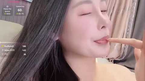 Media: Video of an Asian woman with long, straight black hair, pale skin, and closed eyes, sensually licking her own fingers, wearing a black top.