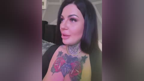 Media: A video of a fair-skinned woman with long black hair, large eyes, and a bold tattoo featuring roses and the word \"LOVE\" on her chest. She wears a black top, standing indoors with a neutral background.