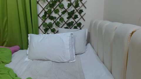 Media: Video of a minimalist, cozy bedroom featuring a white leather headboard, white bedding, green curtains, and a vertical garden with lush green plants against a white wall.