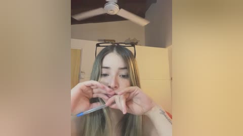 Media: Video of a young woman with long, straight, blonde hair, wearing a light-colored top, using blue scissors to cut a piece of paper into a heart shape.