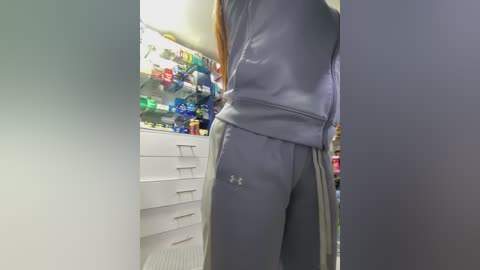 Media: A video shows a person in a gray sweatshirt and sweatpants, standing in a brightly lit, modern kitchen with white cabinets and colorful utensils displayed.