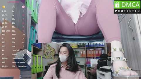 Media: Video of a woman in pink leggings, white shoes, and face mask, sitting in an office with colorful binders and shelves.