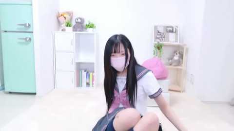 Media: A video of an Asian woman with long black hair, wearing a pink and white school uniform, a face mask, and sitting on the floor in a minimalist, pastel-colored room with a white shelf and stuffed animals.