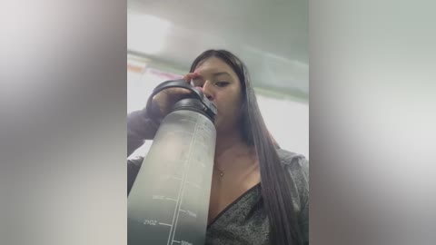 Media: Video of an Asian woman with long black hair, wearing a grey hoodie, drinking from a large, grey water bottle in a gym or locker room.