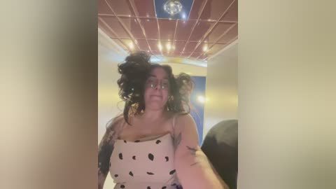 Media: A video of a woman with curly hair, wearing a white top with black polka dots, standing in a dimly lit bowling alley with a red ceiling.