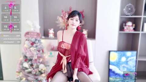 Media: Video of an Asian woman with fair skin, dark hair, and red lingerie, sitting on a couch in a modern living room with a decorated Christmas tree and abstract art.