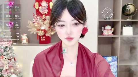 Media: Video of an Asian woman with pale skin, dark hair, and red flower earring, wearing a red shirt, standing indoors with Christmas decorations in the background.